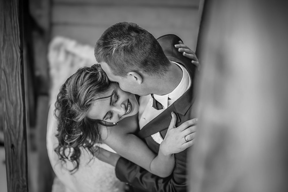 Black and white wedding photo of bride and groom sharing a tender embrace, smiling together.