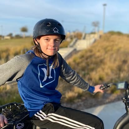 Young girl wearing a helmet rides a BMX bike at an outdoor skate park on a sunny day.