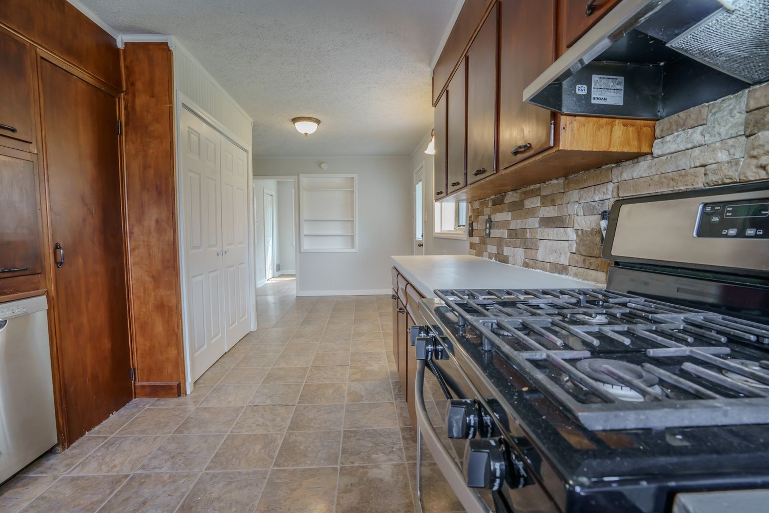 Kitchen with dark wood cabinets, gas range, stone tile backsplash, and beige tile flooring in a residential home.