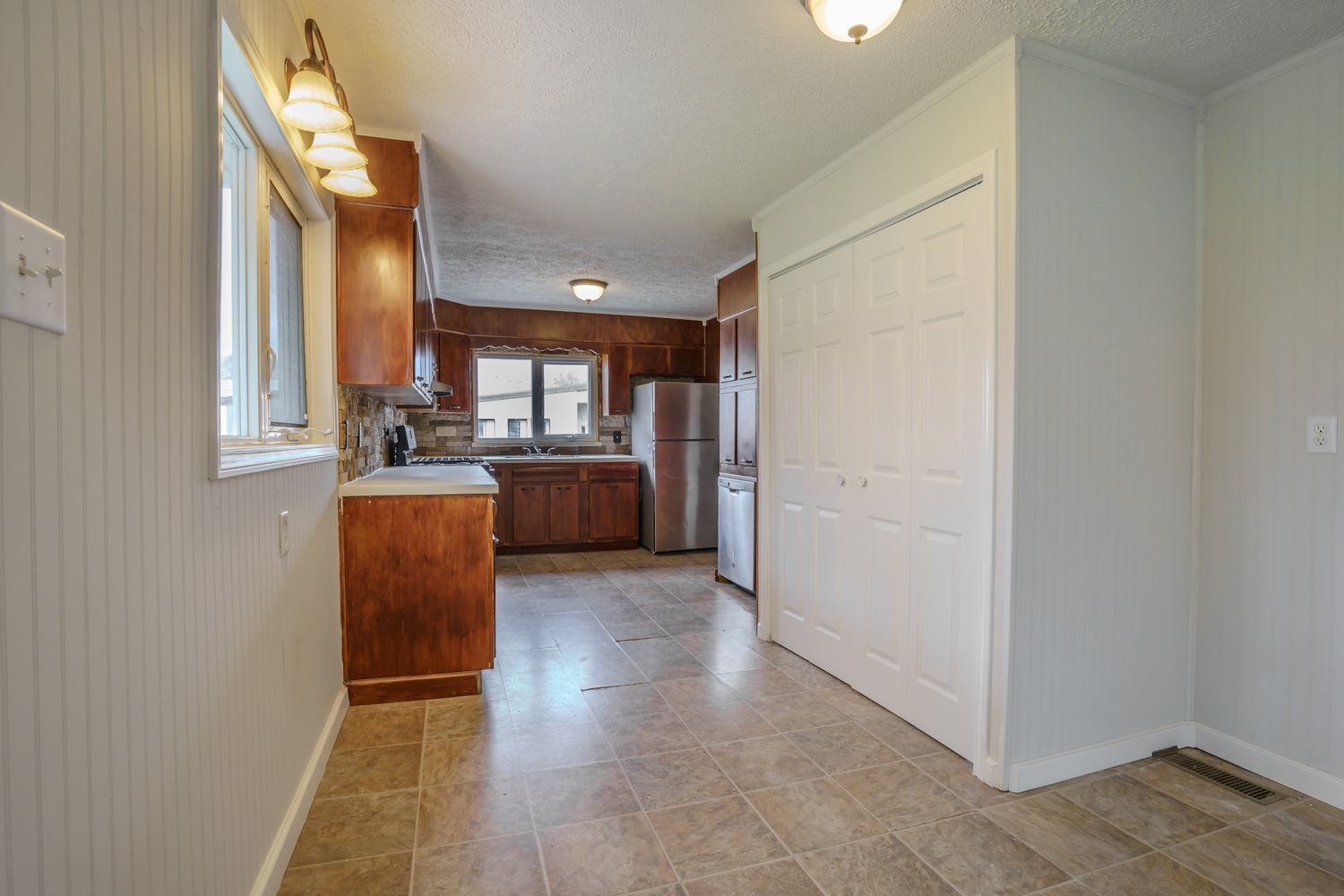 Spacious kitchen with dark wood cabinets, stainless steel refrigerator, tile flooring, and large window over sink.