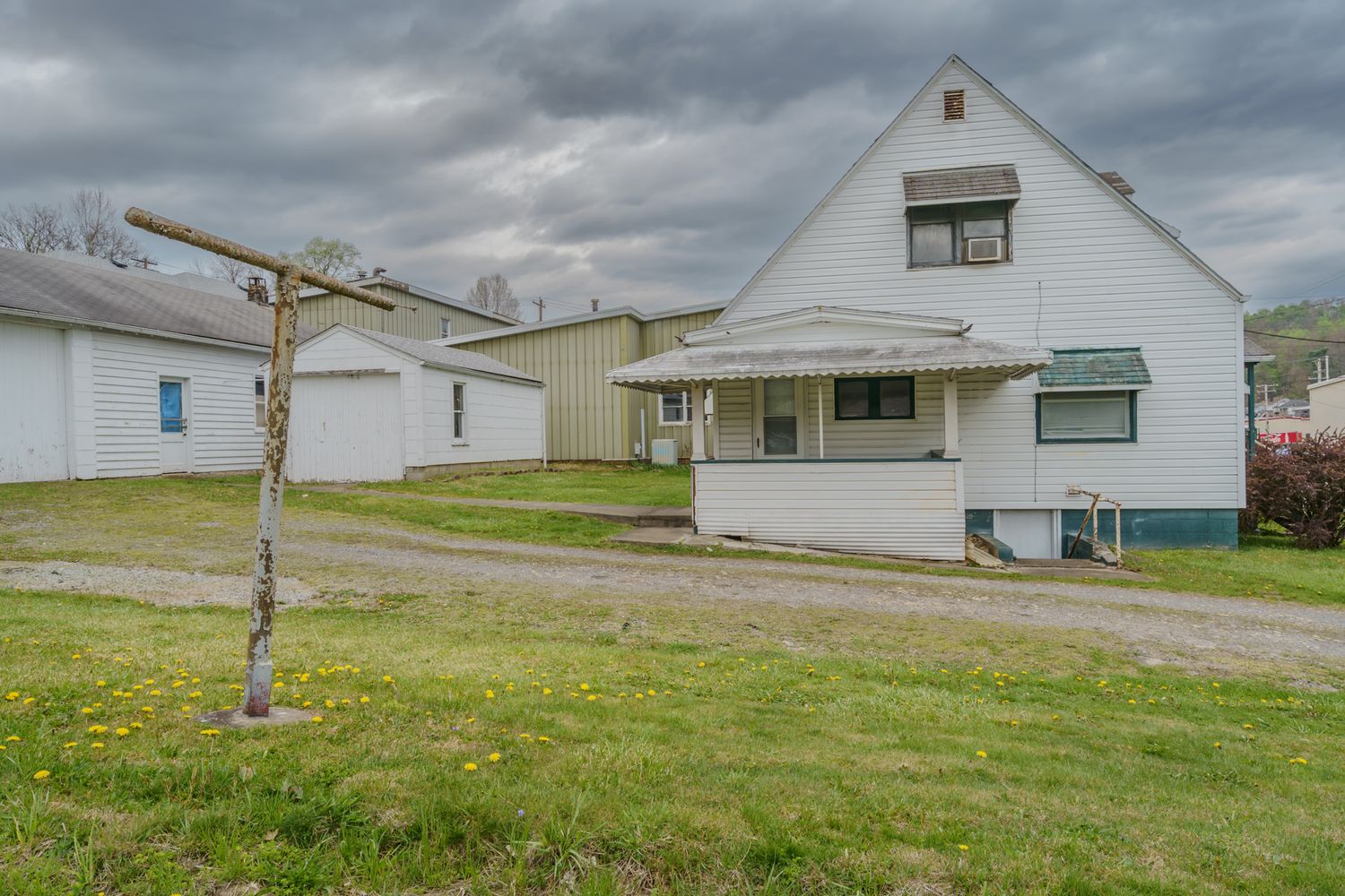 White farmhouse with covered porch, detached garage, and green lawn under cloudy skies.