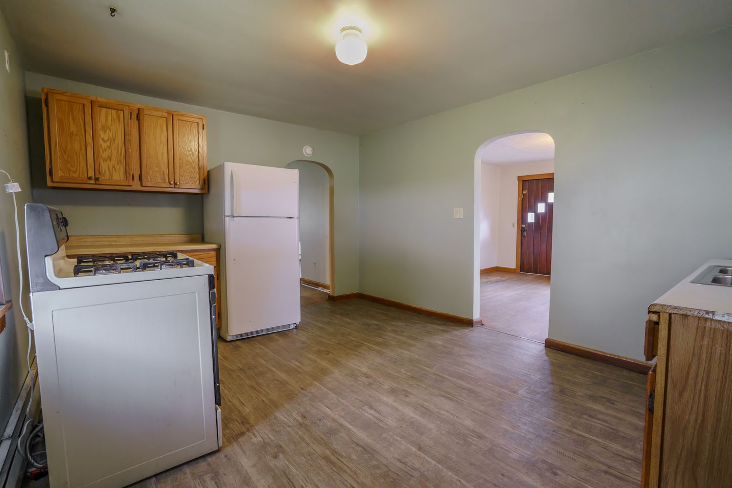 Kitchen with wood cabinets, white refrigerator, gas stove, and arched doorway leading to living area.