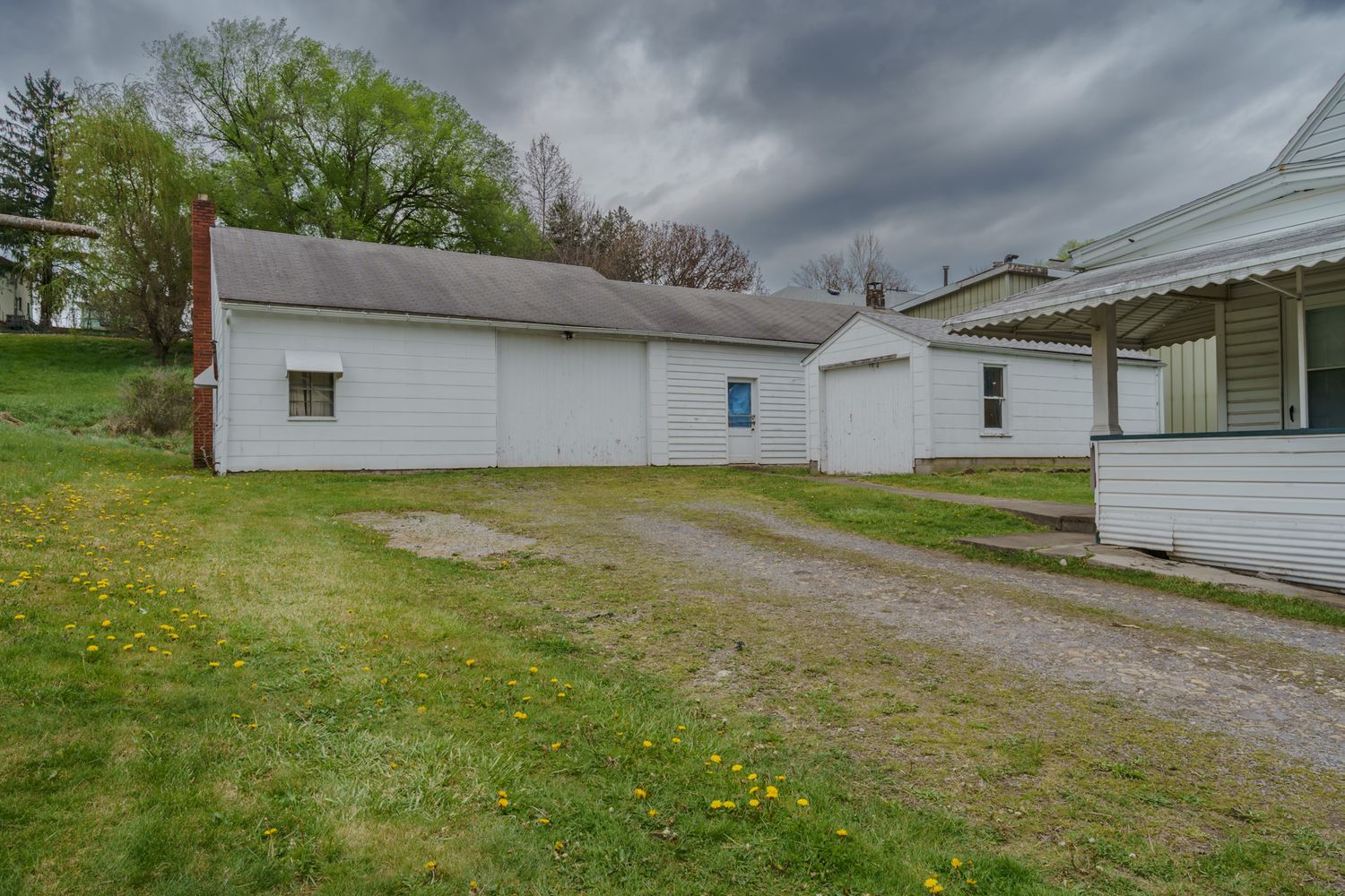 White detached garage and outbuildings with gravel driveway and green lawn on an overcast spring day.