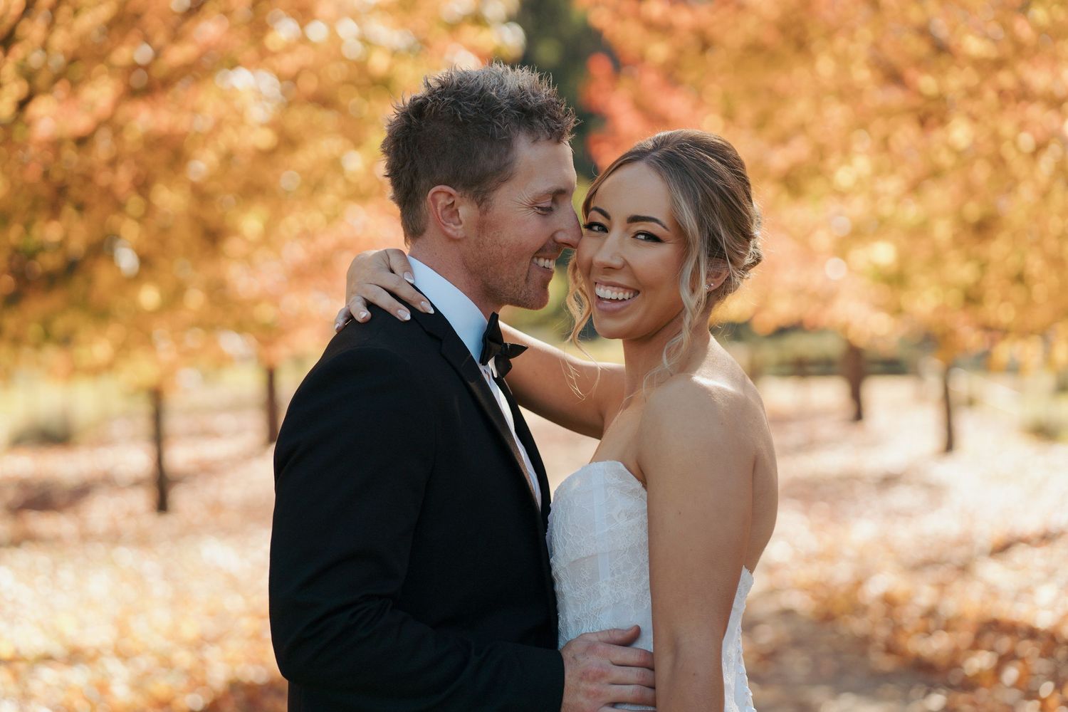 A bride and groom embrace among vibrant autumn foliage, smiling joyfully in an outdoor fall wedding portrait photoshoot in Sydney