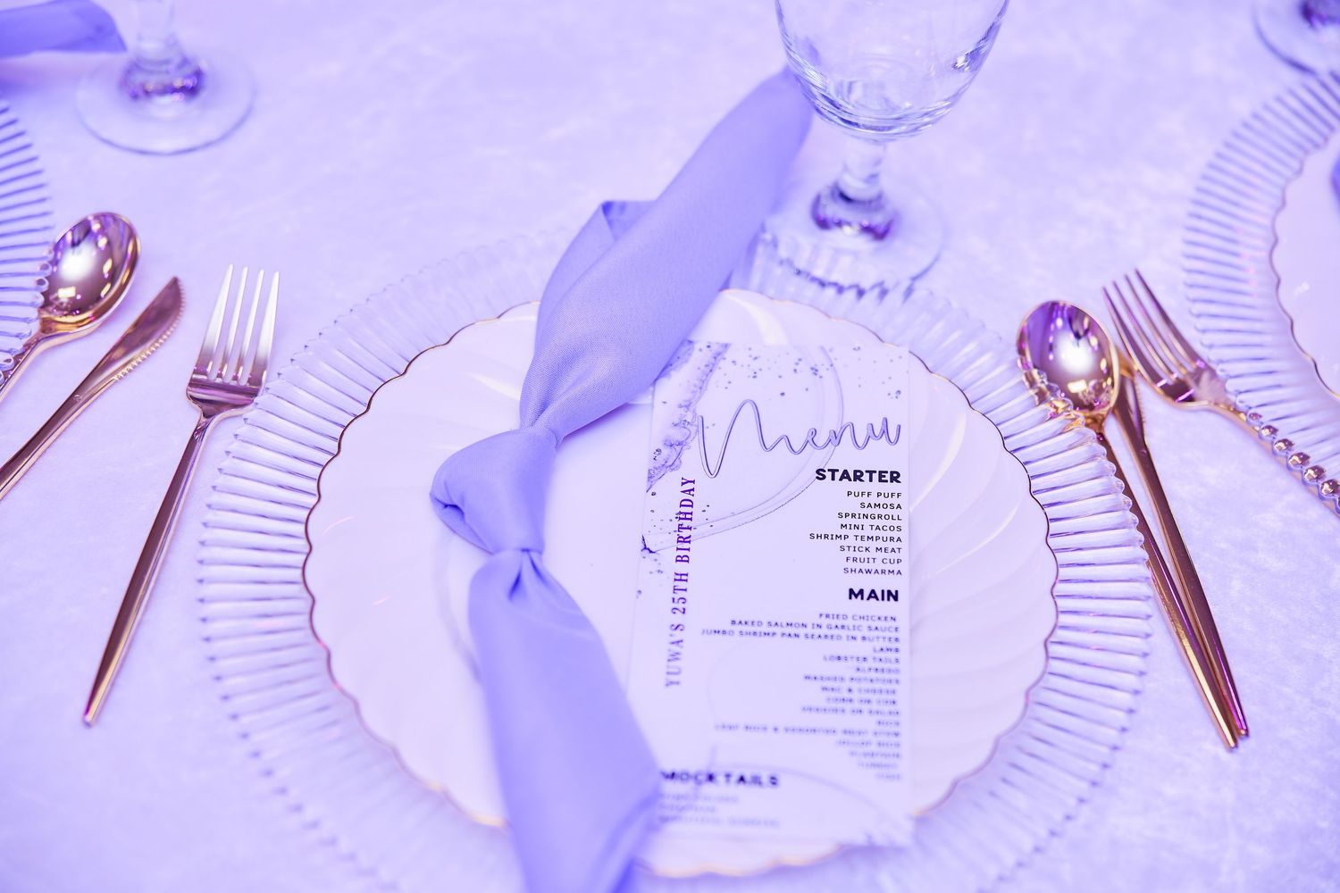 Elegant place setting with lavender napkin, menu card, and rose gold cutlery on white tablecloth.