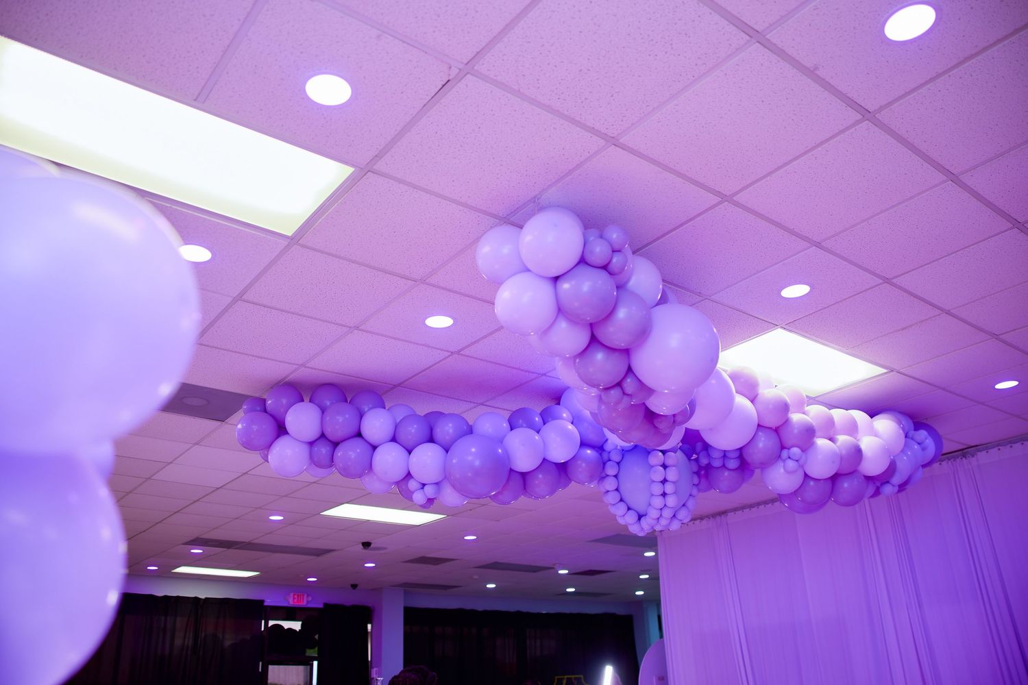 Purple and white balloon garland decorating the ceiling of an elegantly lit event venue.