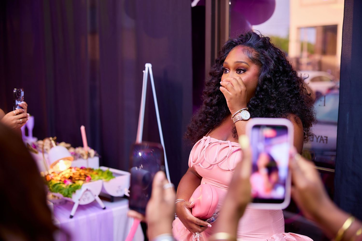 Woman in pink off-shoulder dress looking surprised at her baby shower celebration.