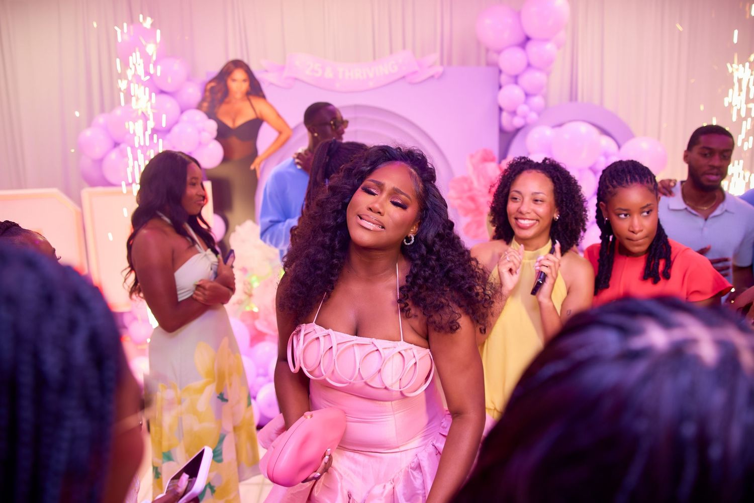 Woman in pink dress smiling at elegant purple-themed birthday party celebration with guests.