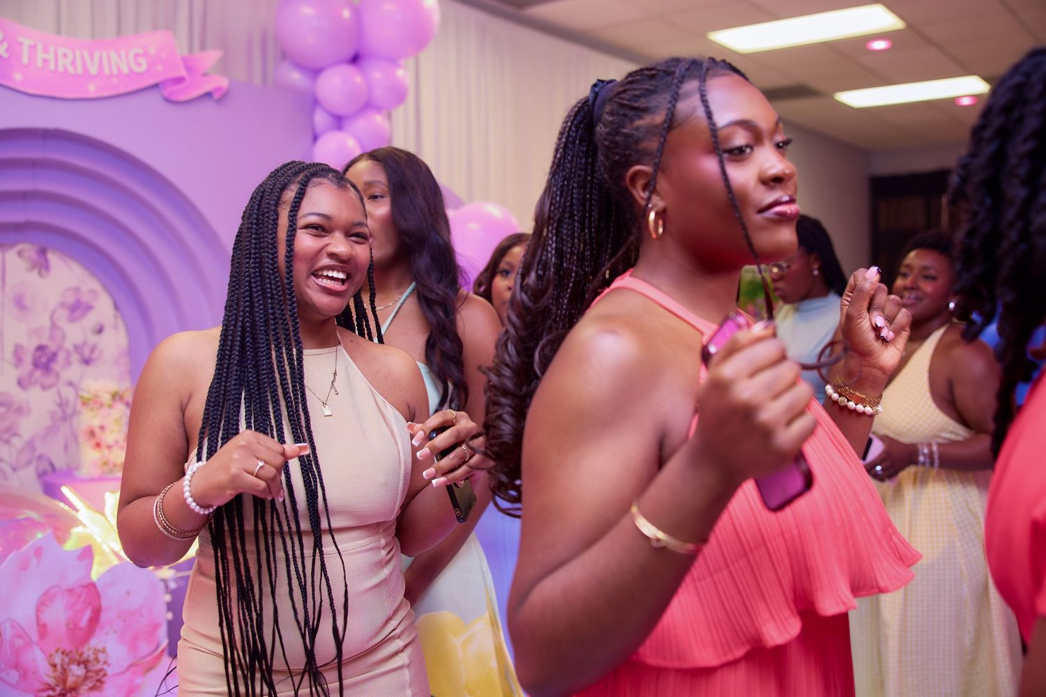Guests dancing and celebrating at a purple-themed birthday party, wearing pink and white outfits in a decorated venue.