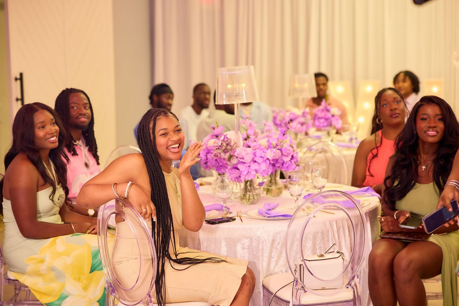 Group of women laughing at decorated table with purple flowers at a birthday party.