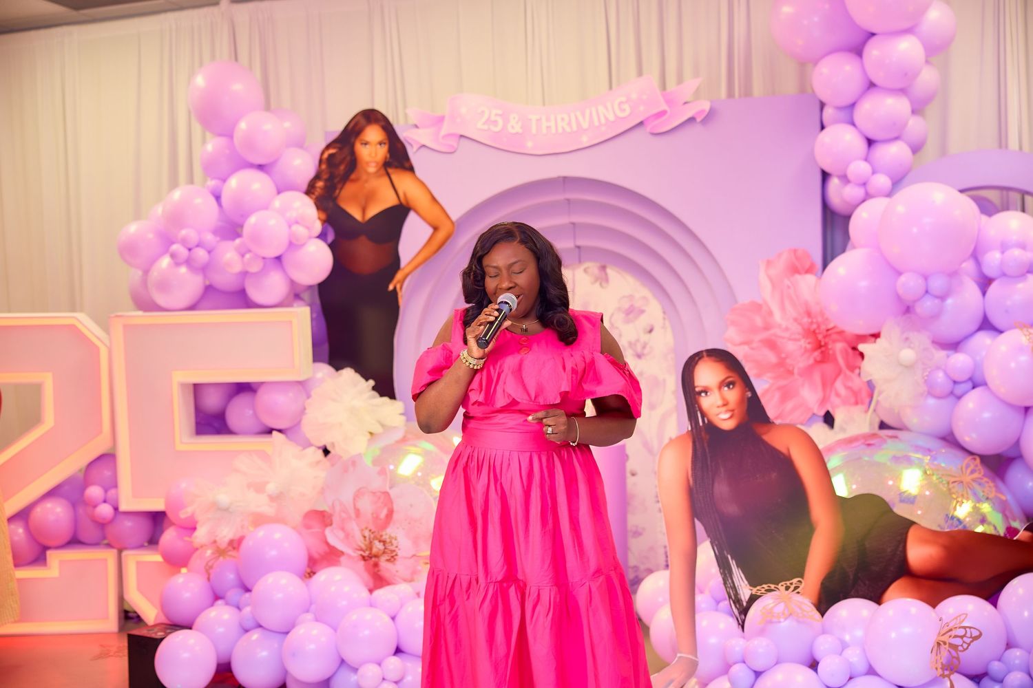 Woman in hot pink dress singing at microphone at a 25th birthday party celebration.