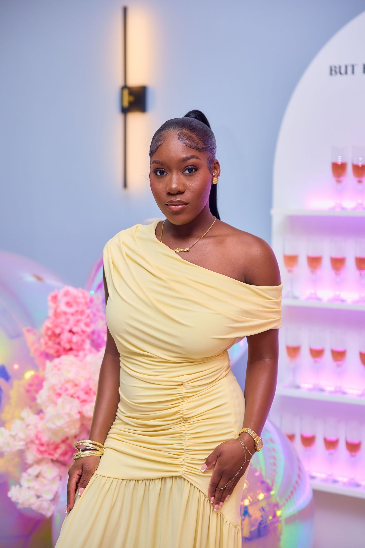 Young woman in yellow off-shoulder dress posing near champagne display at event.