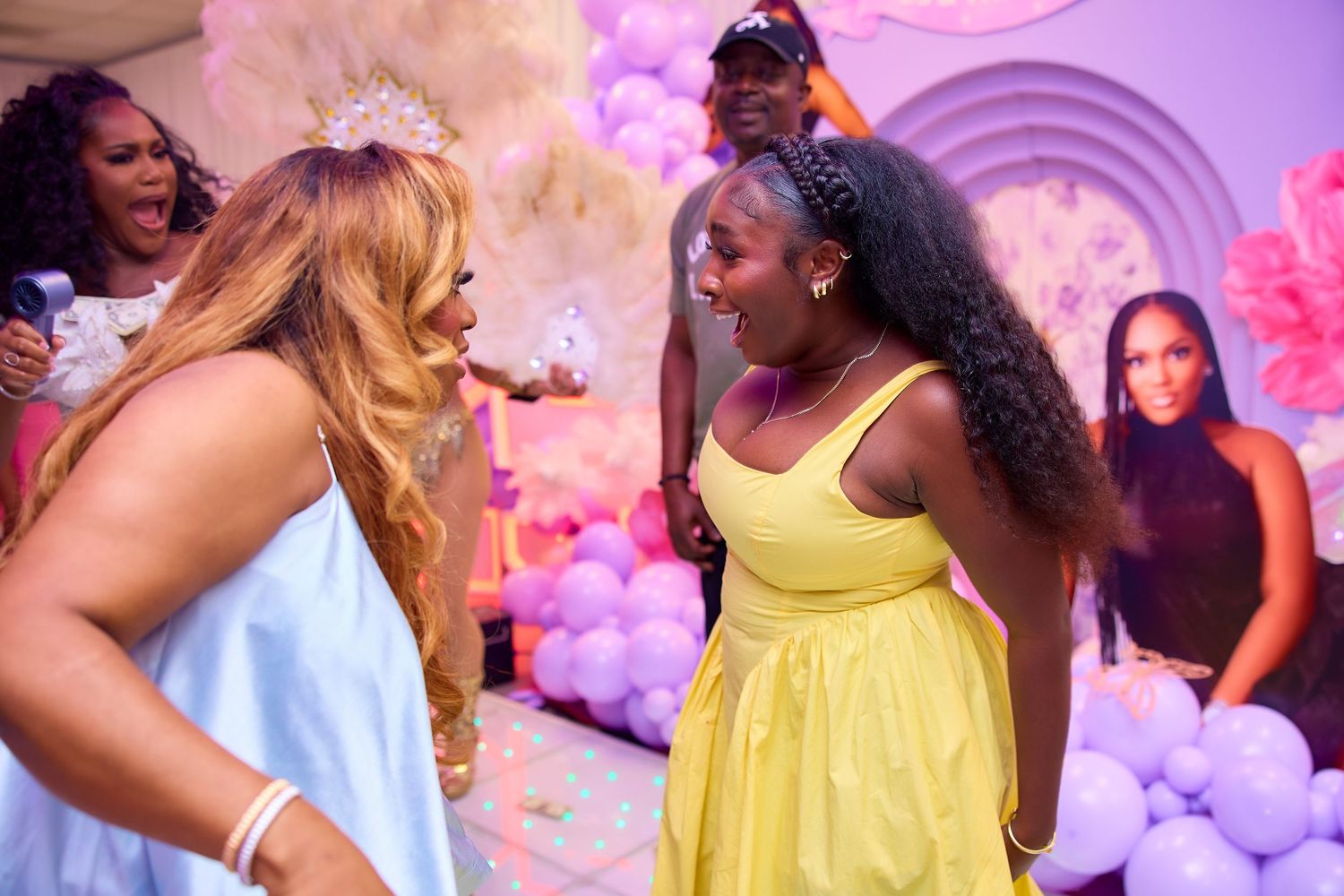 Two women laugh together at colorful balloon-decorated birthday party celebration.
