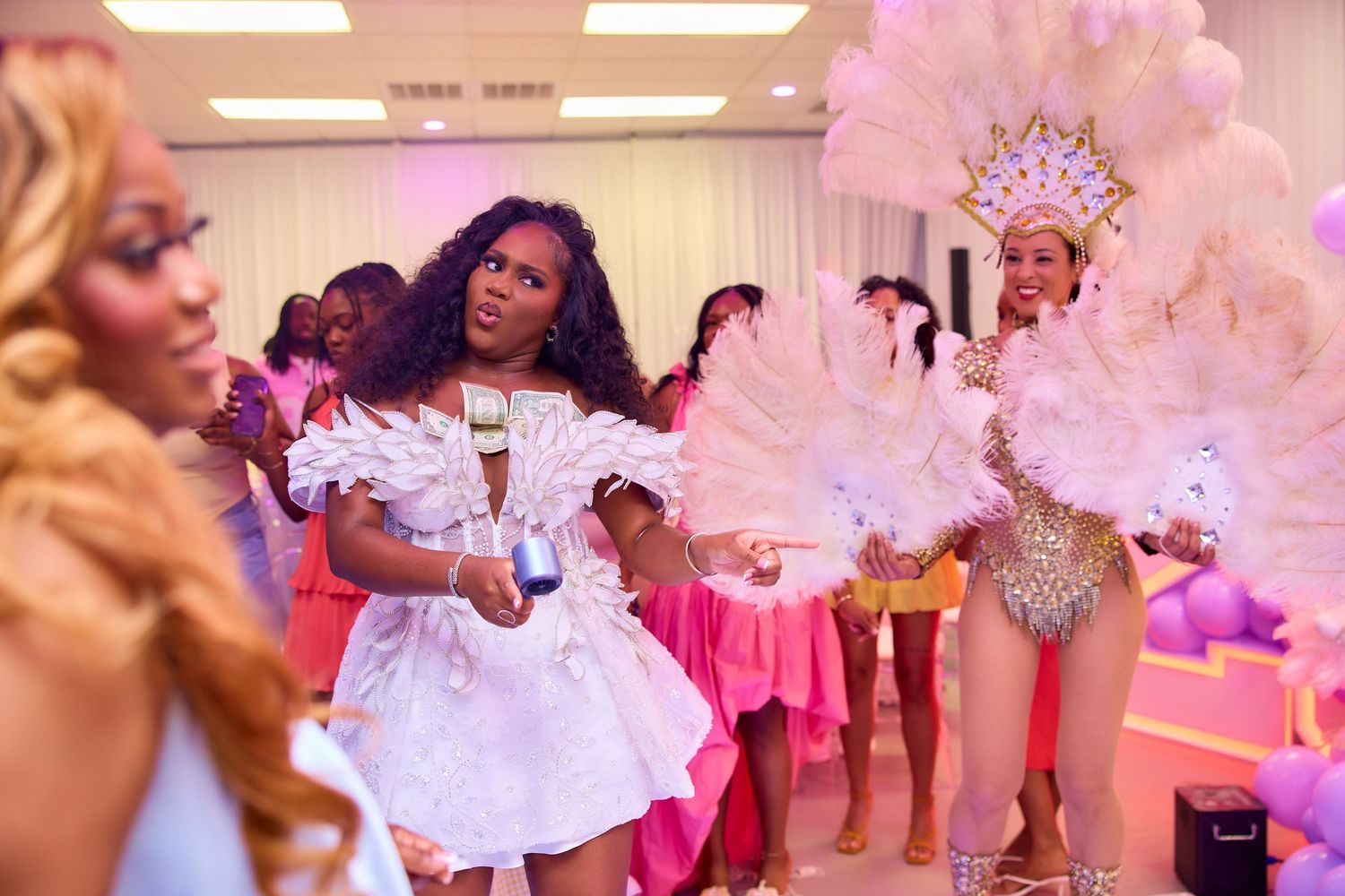 Woman in white dress dancing with showgirl performer in feathered costume at birthday party.