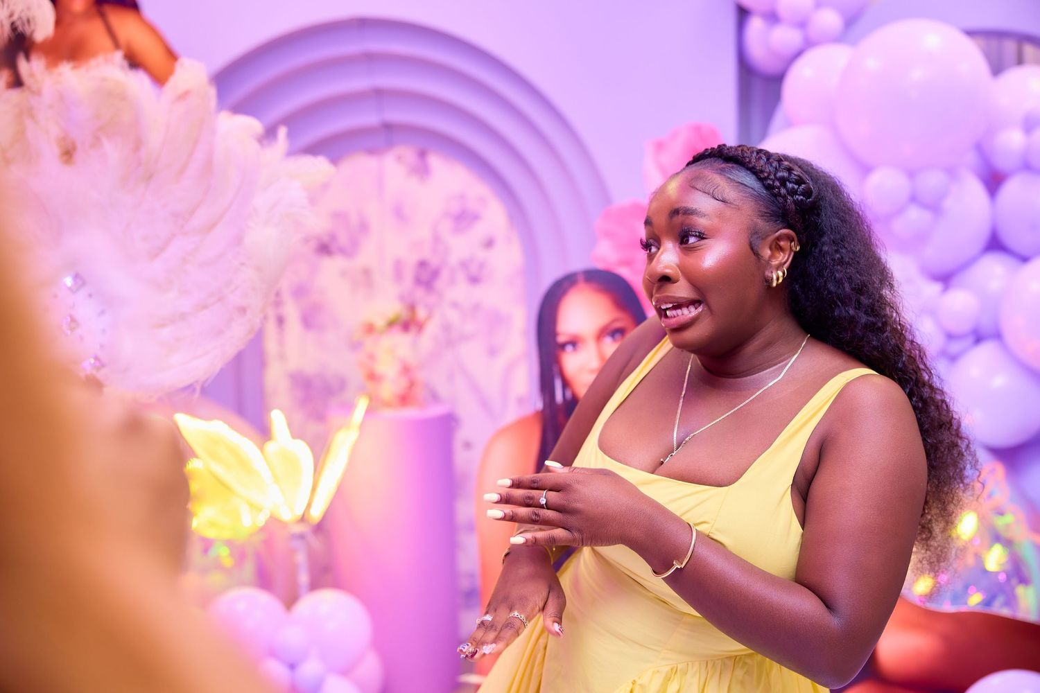 Young woman in yellow dress gesturing at a colorful balloon-decorated birthday party event.