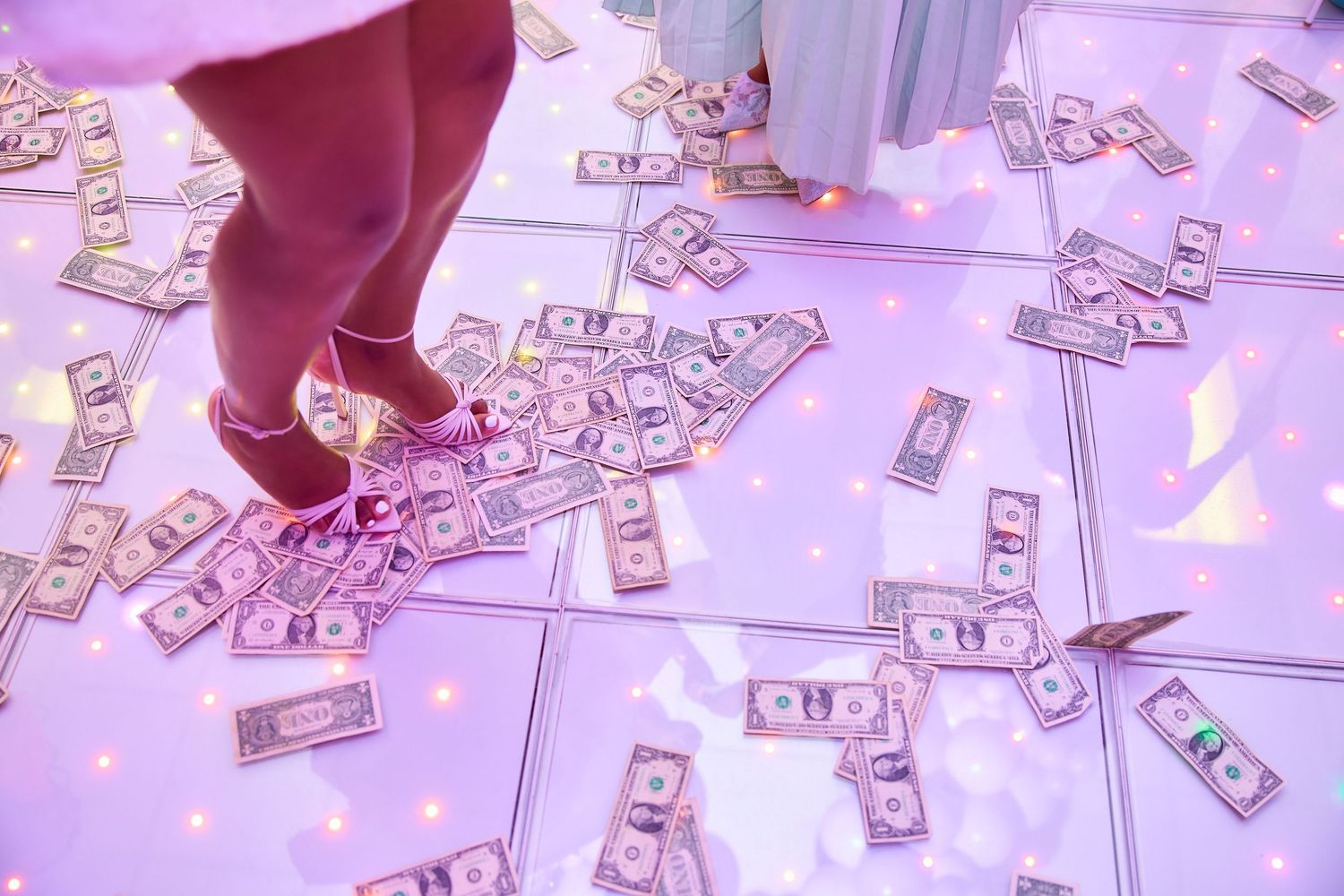 Dollar bills scattered across a glowing dance floor at a festive party event.