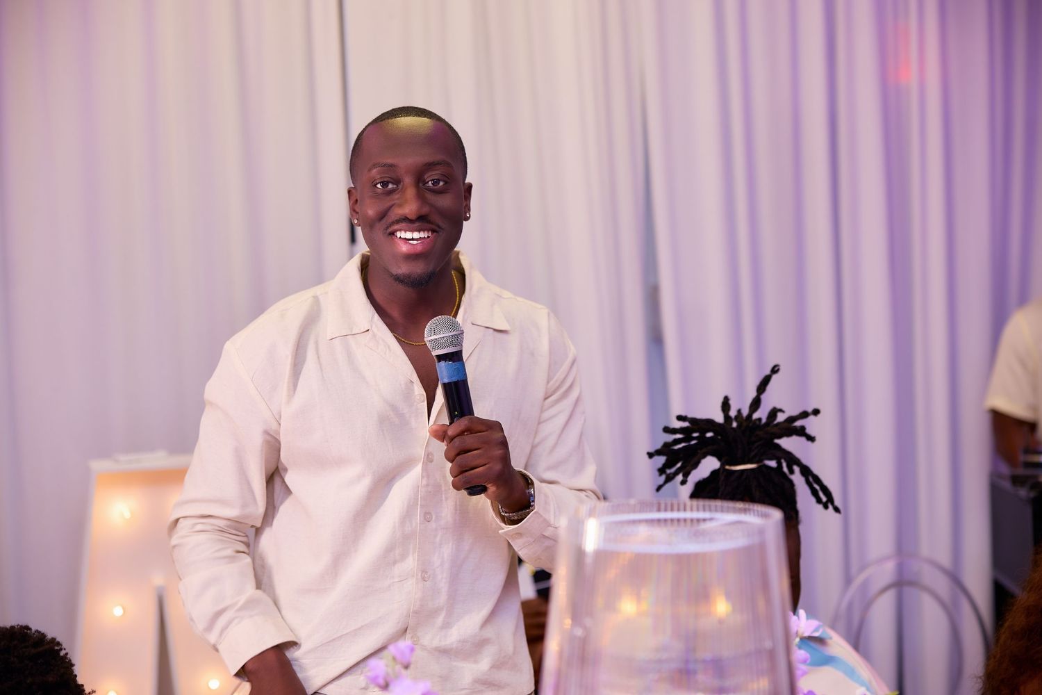 Smiling man in white shirt holding microphone at an elegant event celebration.