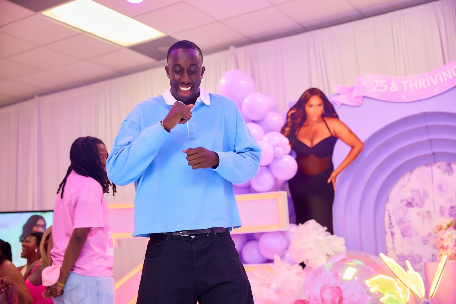 Man in blue shirt dancing at purple balloon decorated birthday party venue.