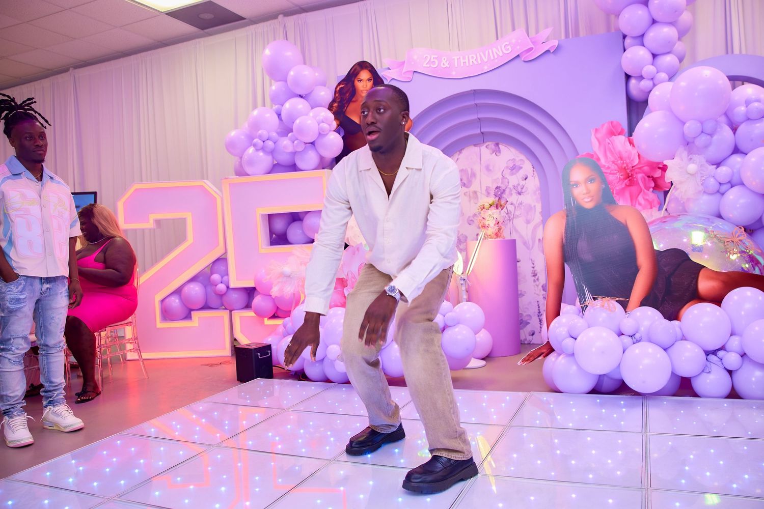 Man dancing on lit dance floor at a purple balloon-decorated 25th birthday party.