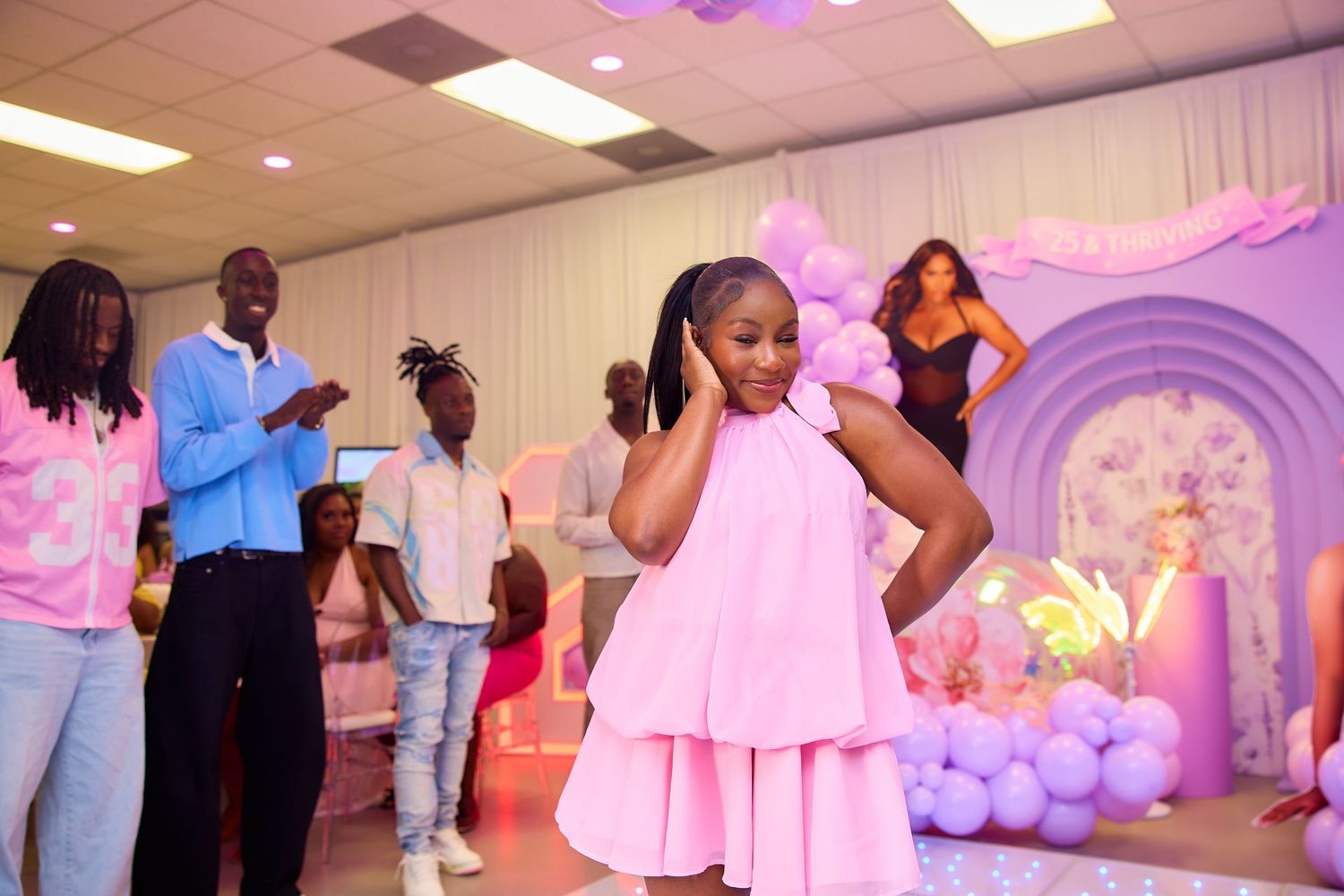 Young girl in pink dress dancing at purple balloon decorated birthday party venue.