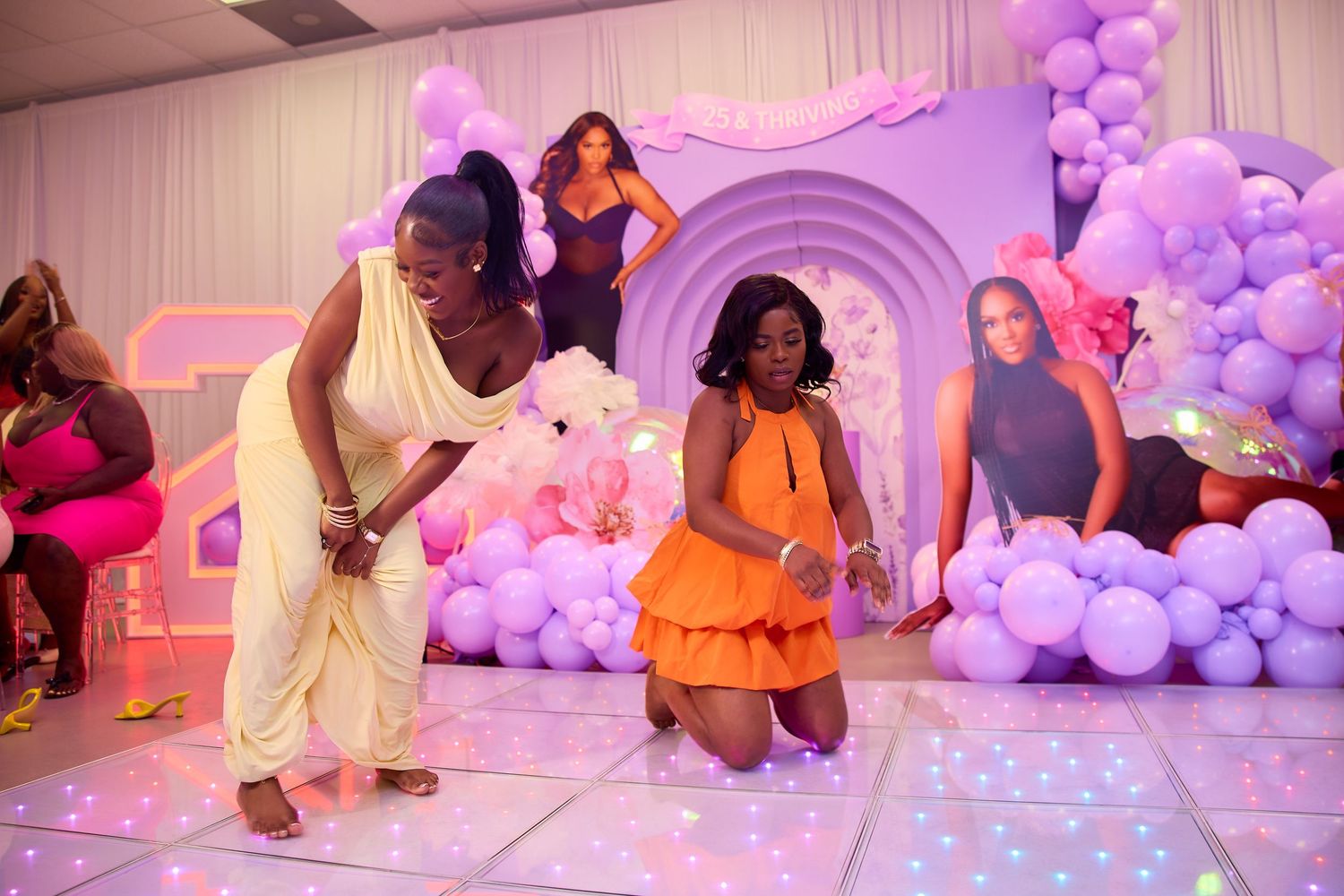 Two women dancing on a lit dance floor at a vibrant purple-themed celebration party.