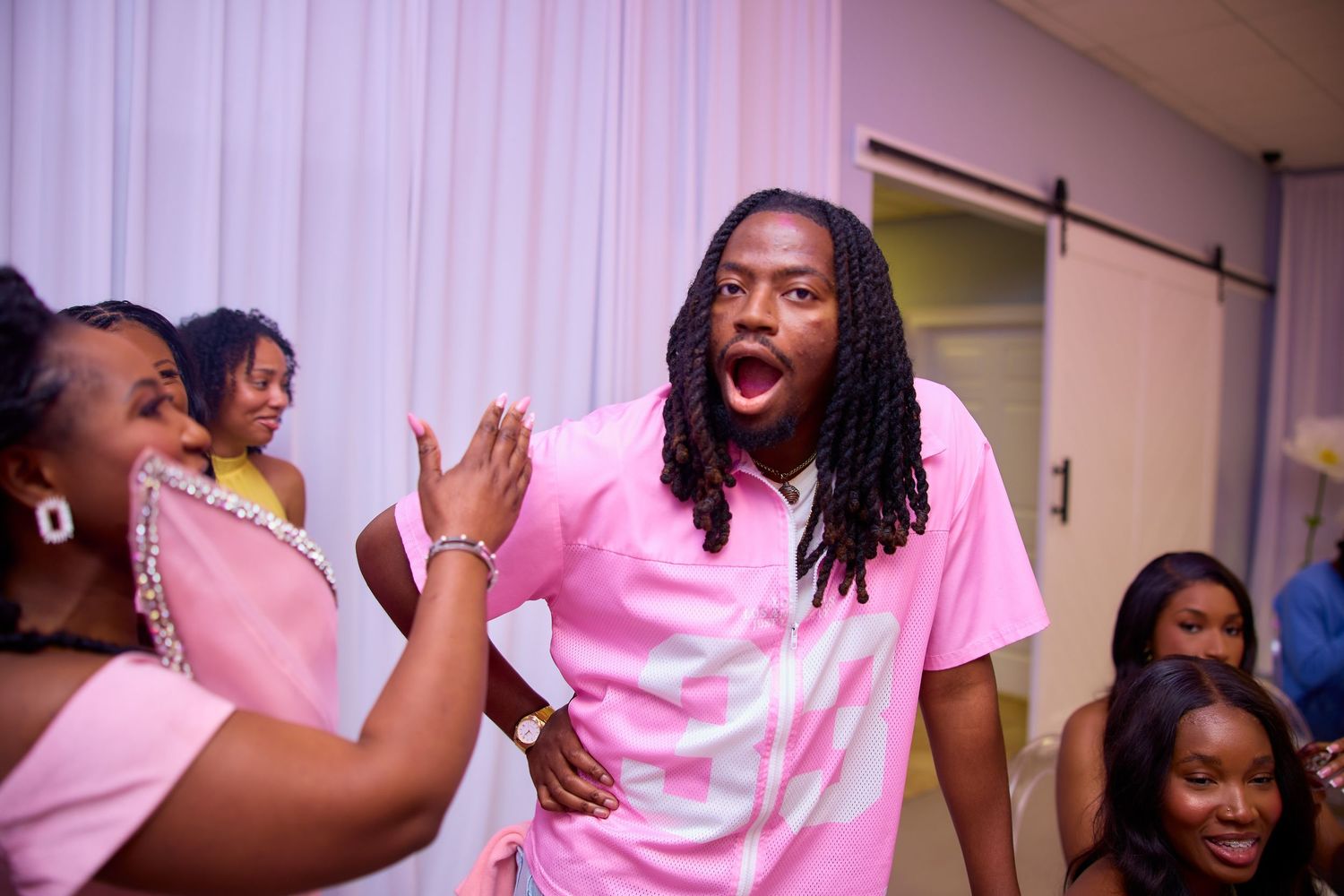Man in pink shirt reacts excitedly while high-fiving woman at a birthday celebration.