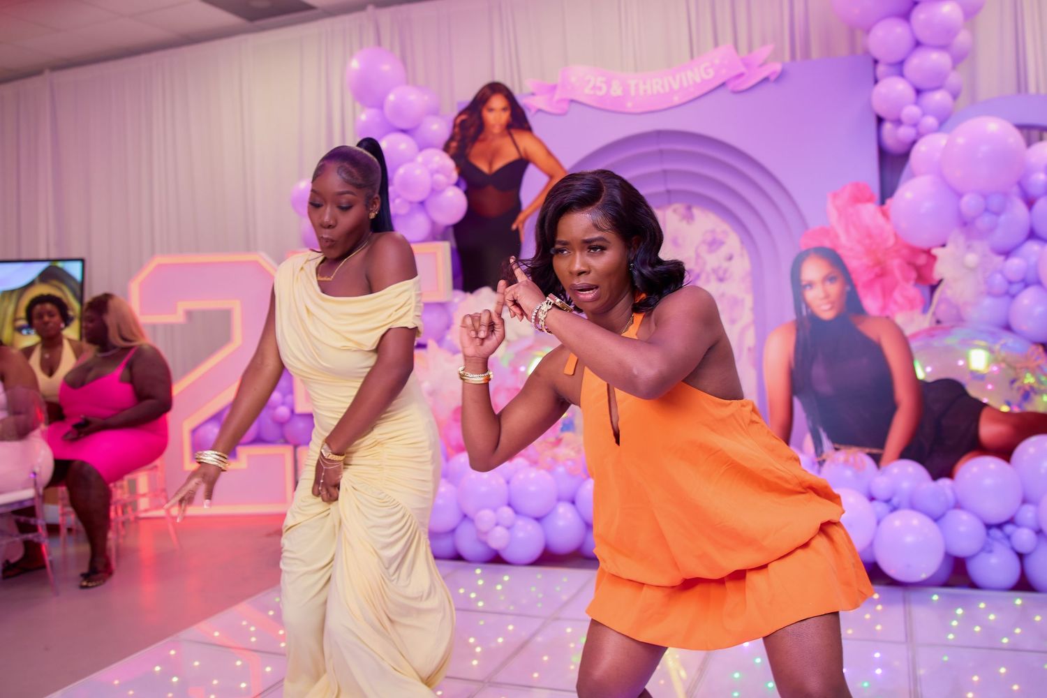 Two women dancing together on illuminated floor at purple and white themed birthday party.