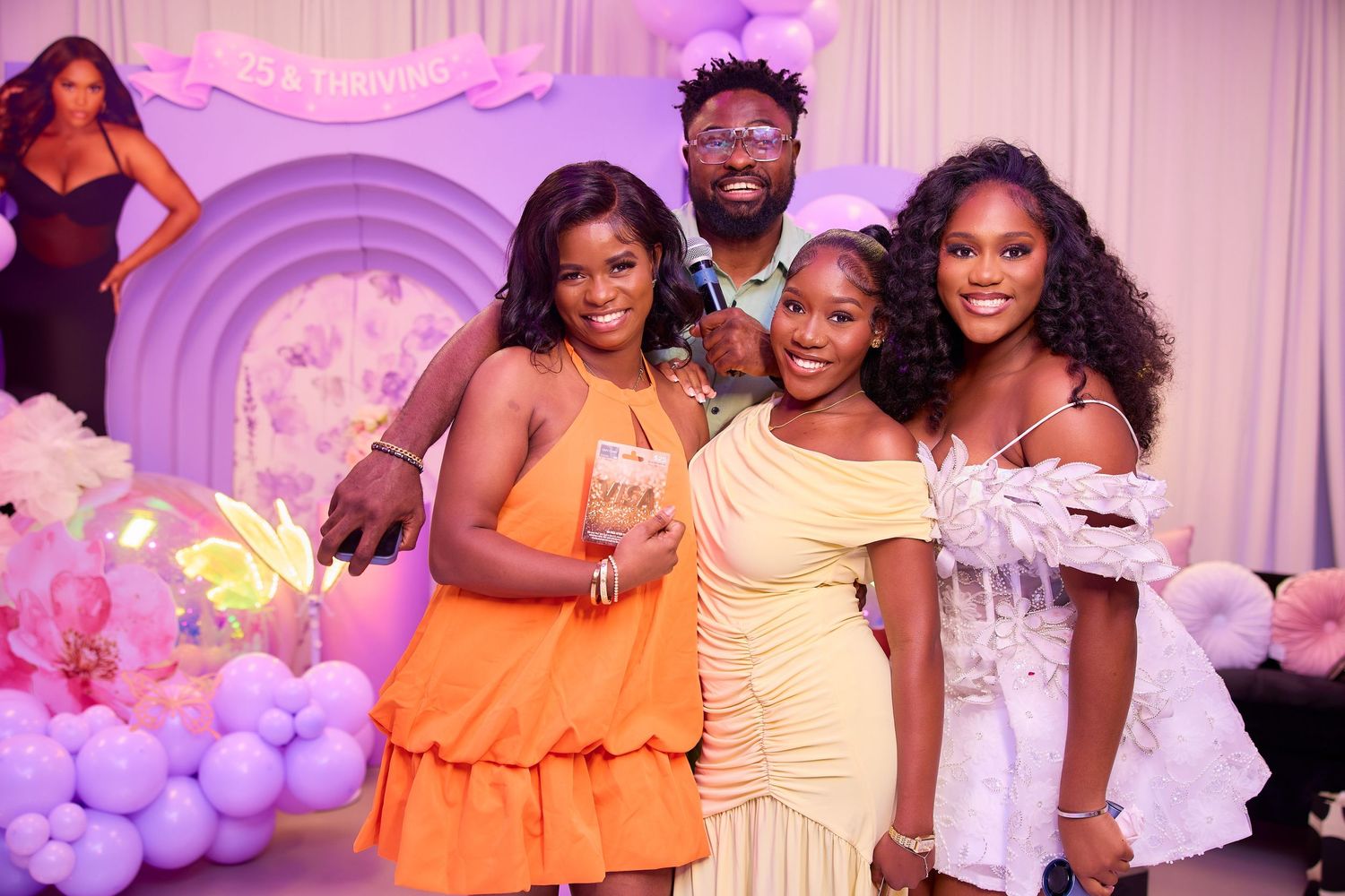 Four friends pose together at a purple-themed birthday party with balloon decorations and festive backdrop.