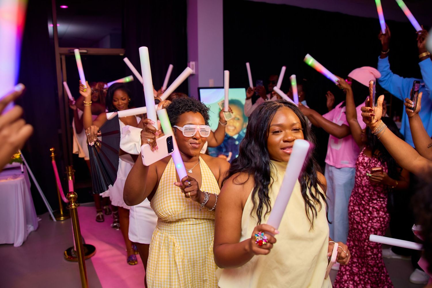 Guests celebrate at a party holding colorful LED glow sticks while wearing fun glasses at an indoor event.