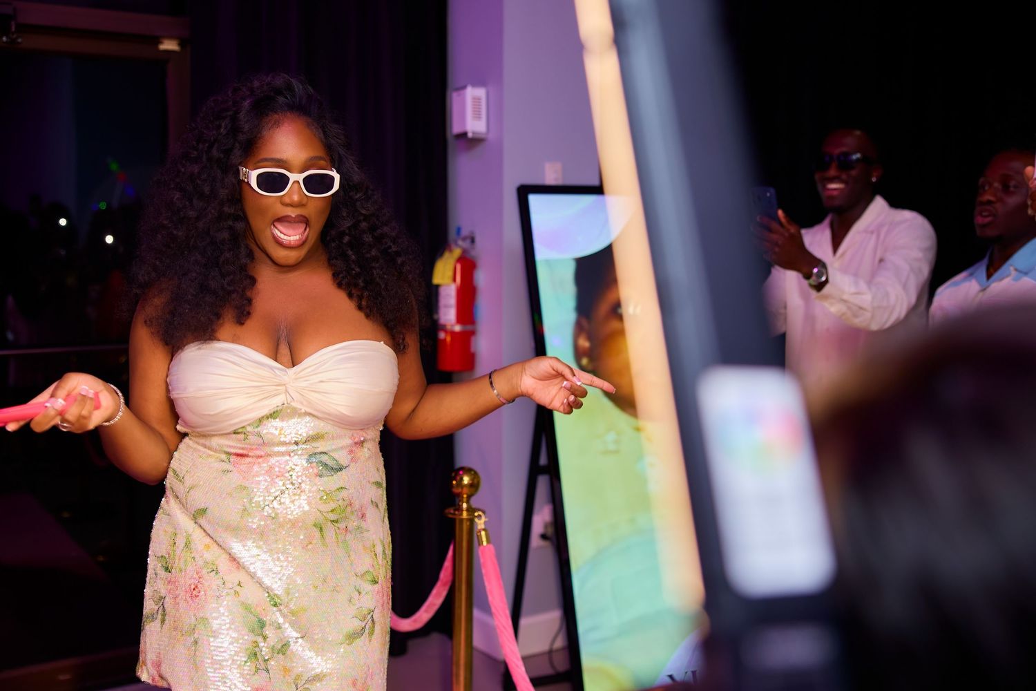 Woman in floral dress and white sunglasses smiling at a photo booth at an elegant evening event.