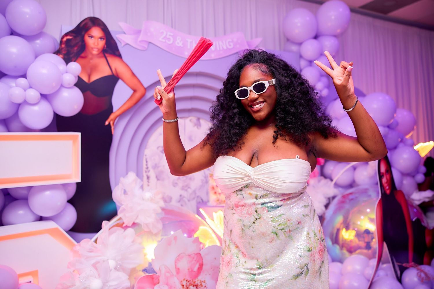 Woman poses in white dress at purple balloon-decorated Nicki Minaj themed birthday party.
