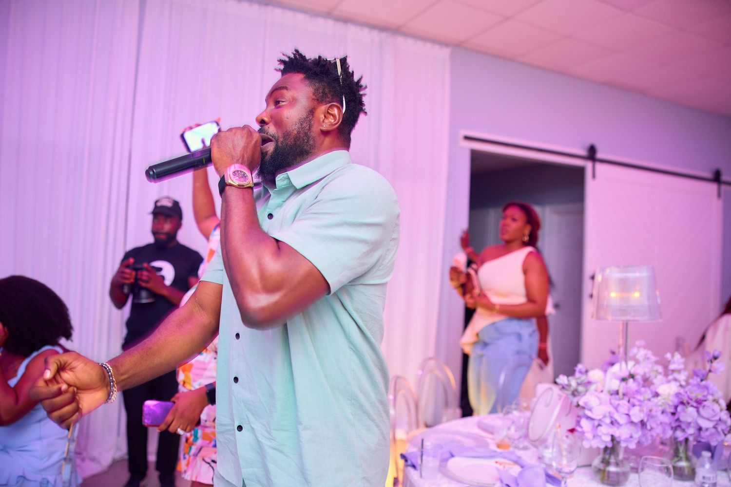 Male performer sings into microphone at elegant purple and white decorated event.