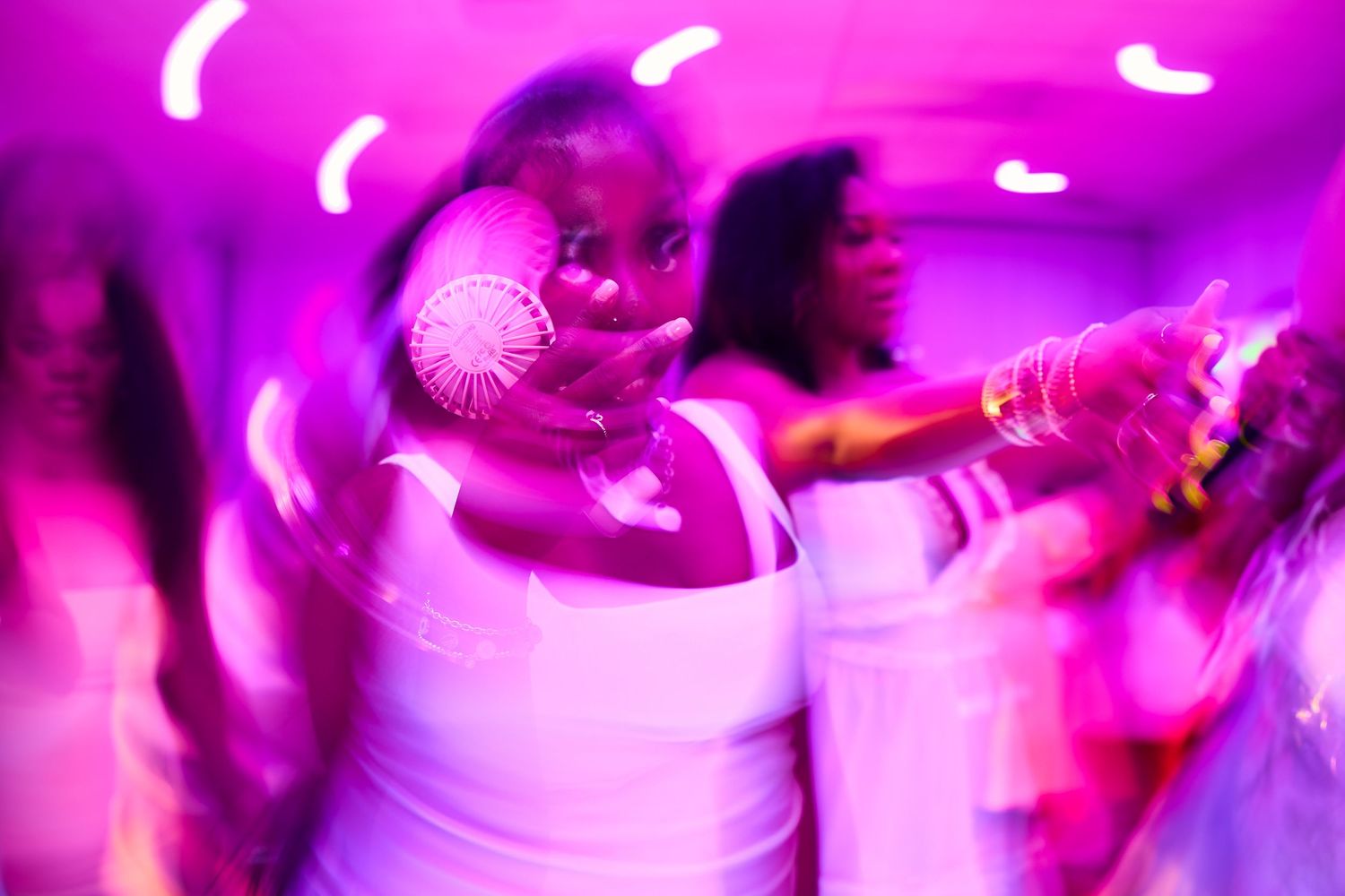 Woman dancing with fan under pink neon lights at lively party event.