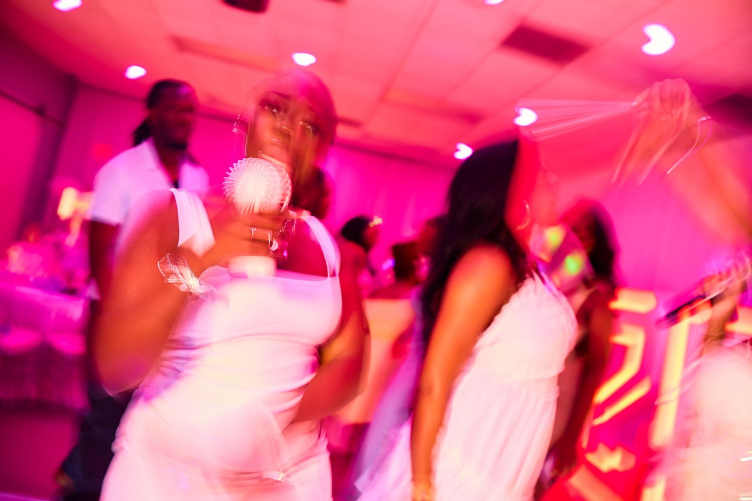 Women in white dresses dancing under pink lights at a lively party event.