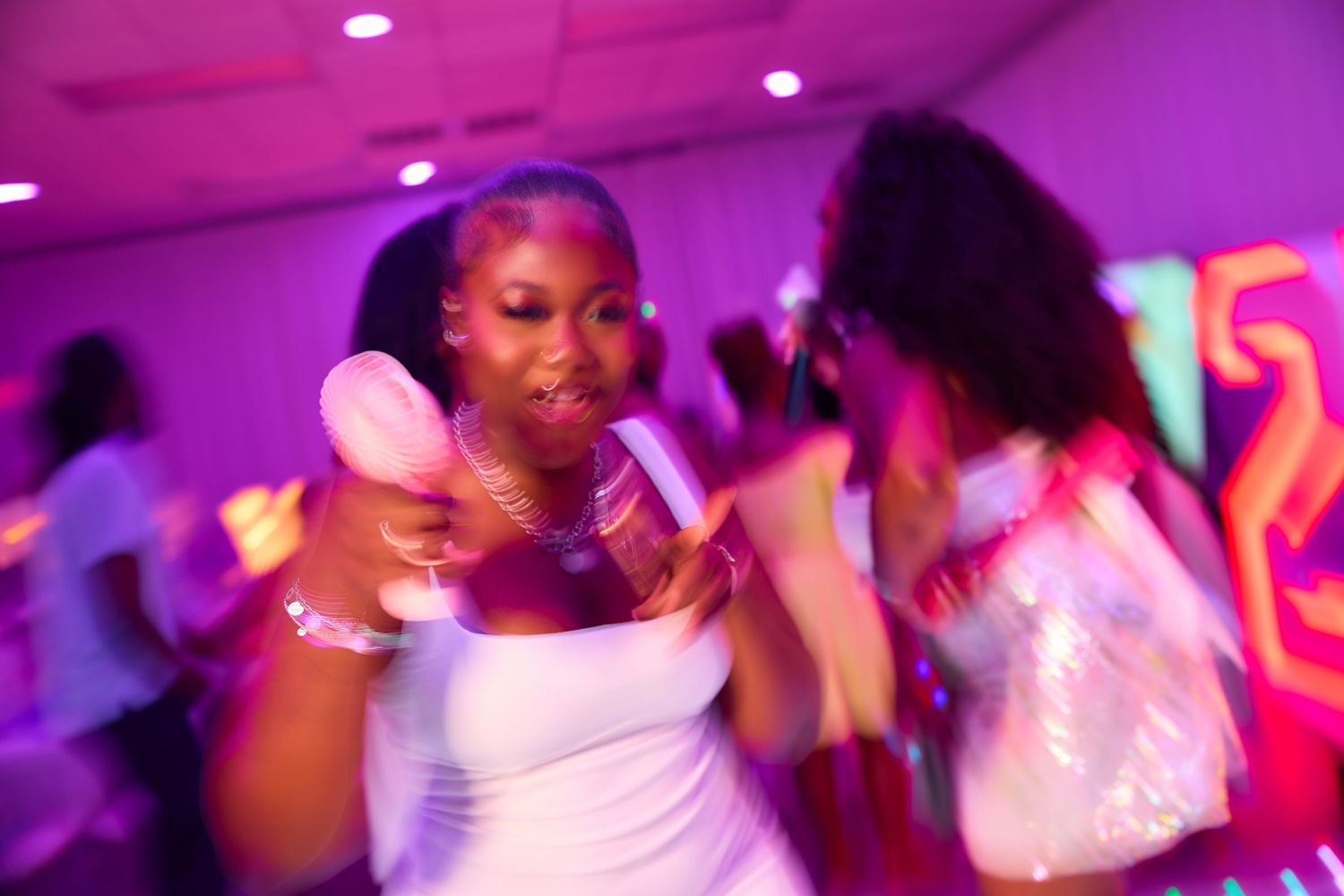Women dance energetically under pink neon lights at a lively celebration party.