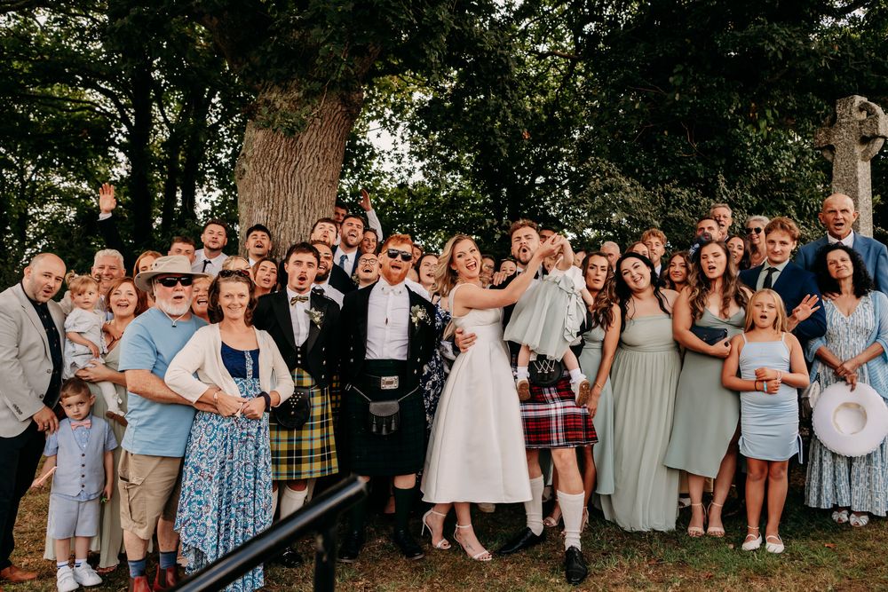 Outdoor wedding ceremony with guests sitting on benches beneath tall trees in a park setting during golden hour.