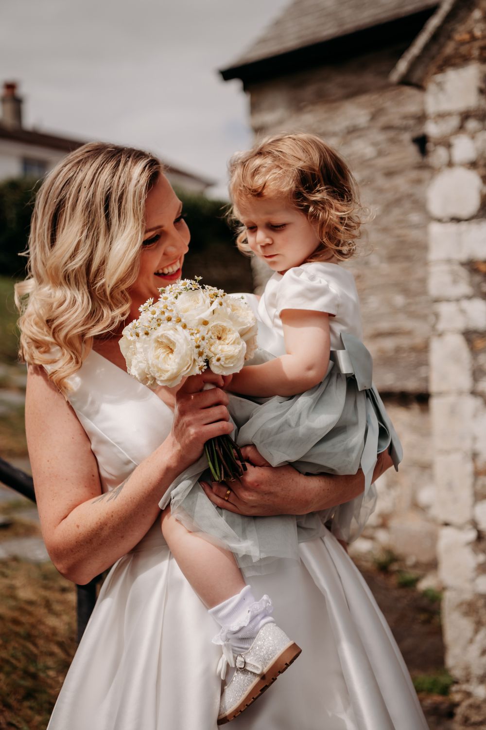 A series of tender moments between a woman in white and a small child in gray against a rustic stone wall backdrop.