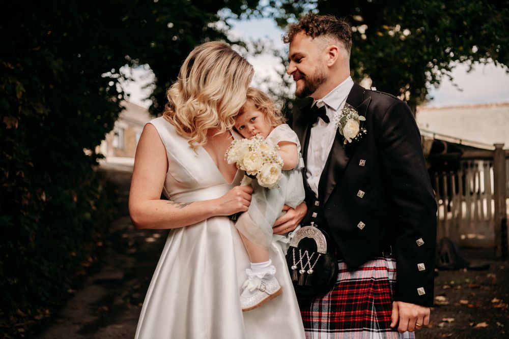 A couple shares a joyful moment at their wedding, the groom wearing a traditional Scottish kilt and bride holding white flowers.