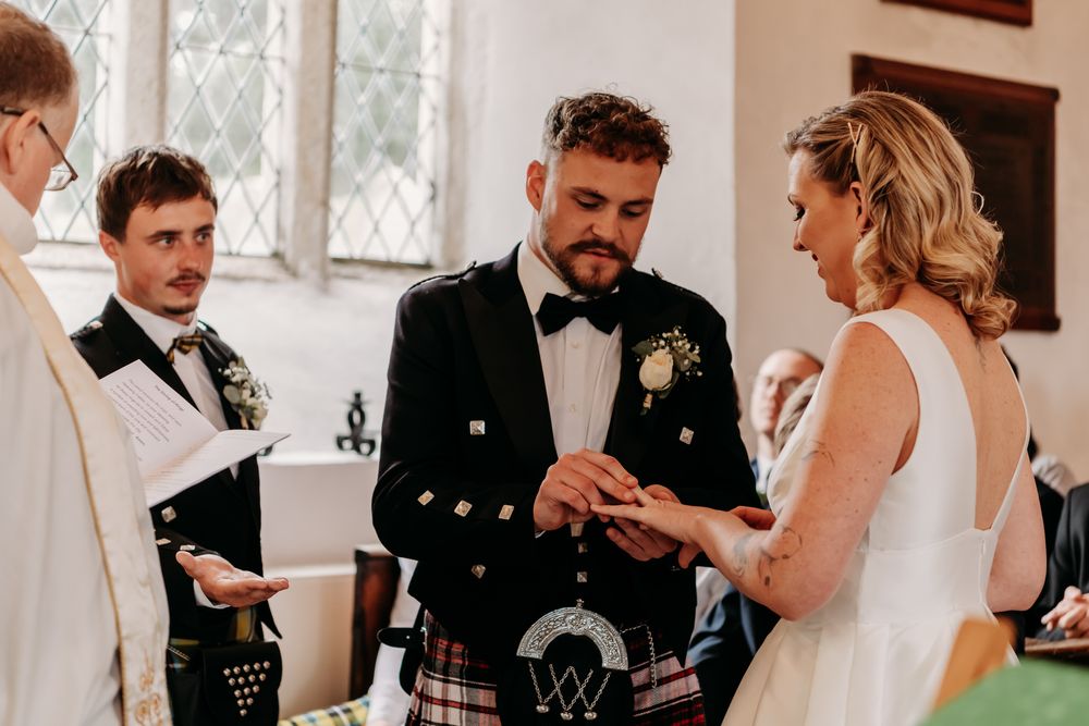 Couple exchanges rings during traditional Scottish wedding ceremony in beautiful church setting with kilts and formal attire.