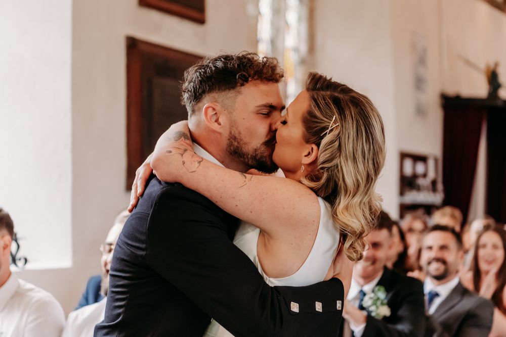 Wedding guests celebrate and smile as they watch an intimate ceremony moment unfold inside a church venue.