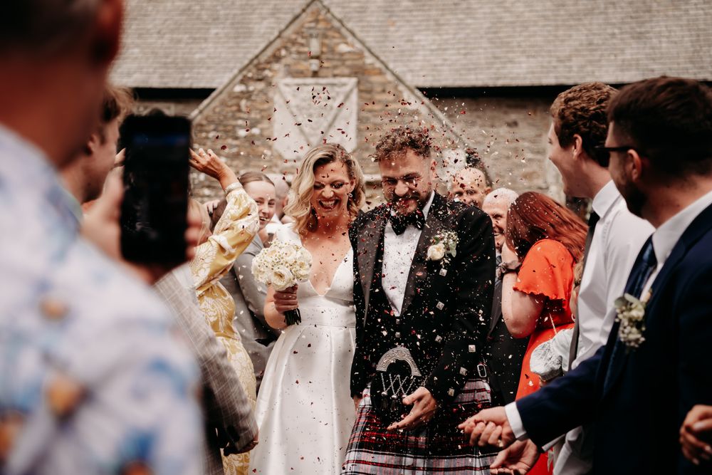 Wedding guests throw confetti over a newly married couple exiting a church while celebrating their special day.