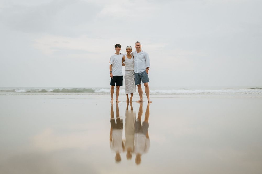 Three people standing on reflective wet sand at the beach during cloudy weather.