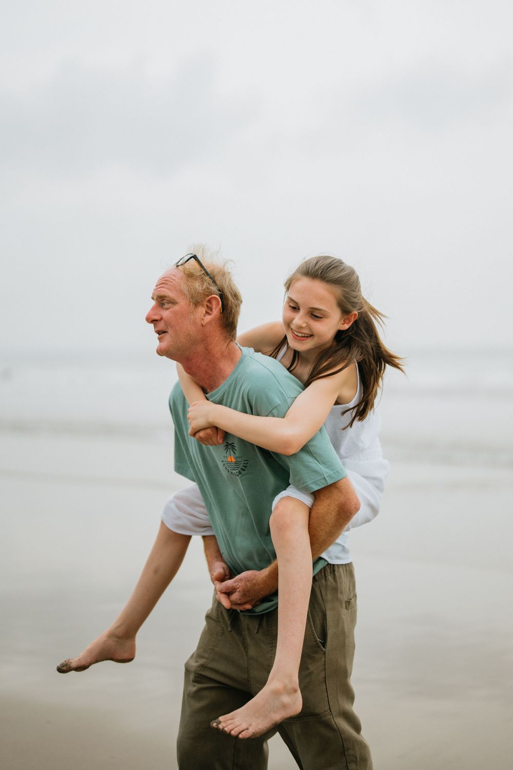 Playful piggyback ride moment captured on a cloudy beach.