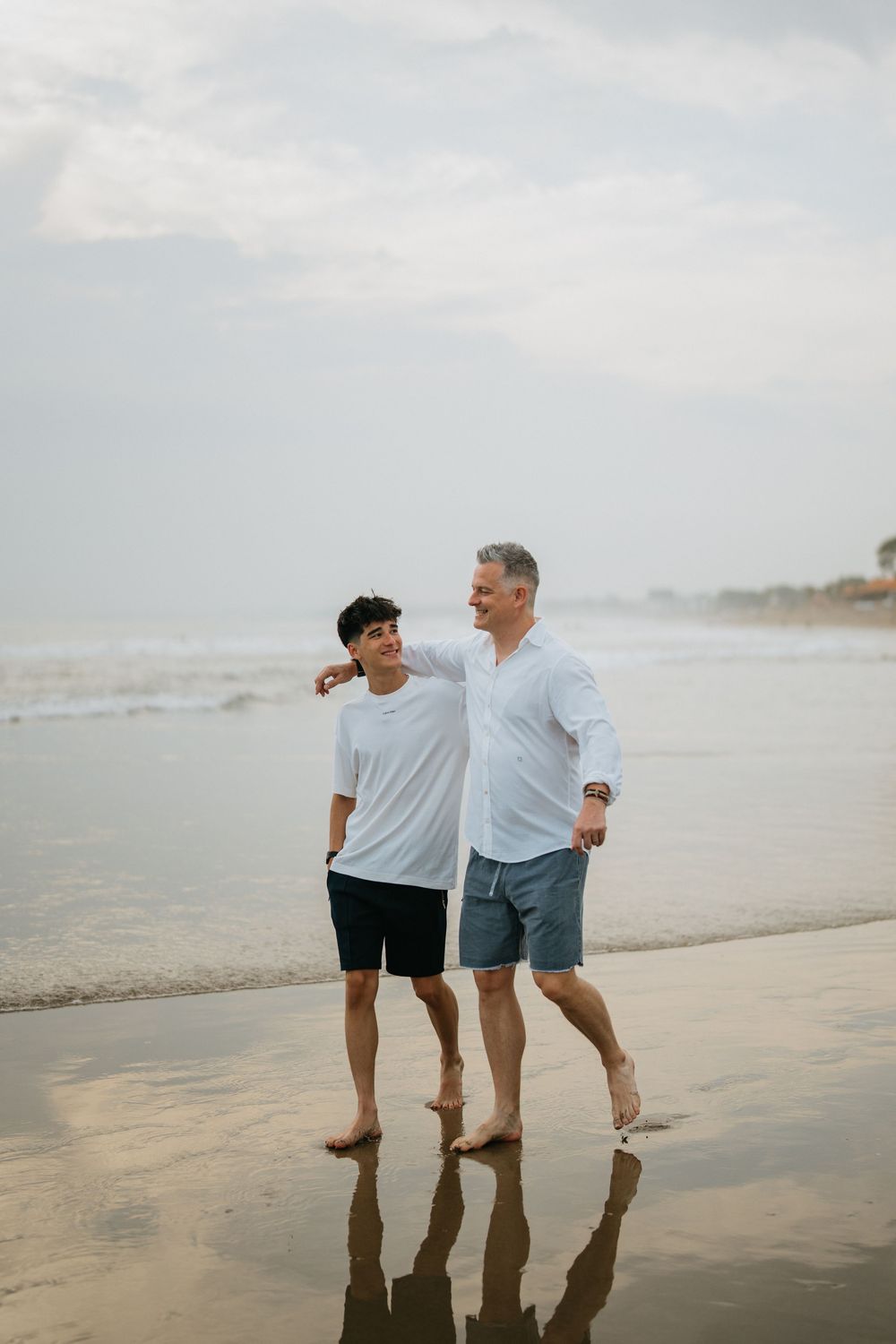 Two people walking together on wet sand at the beach during overcast weather.