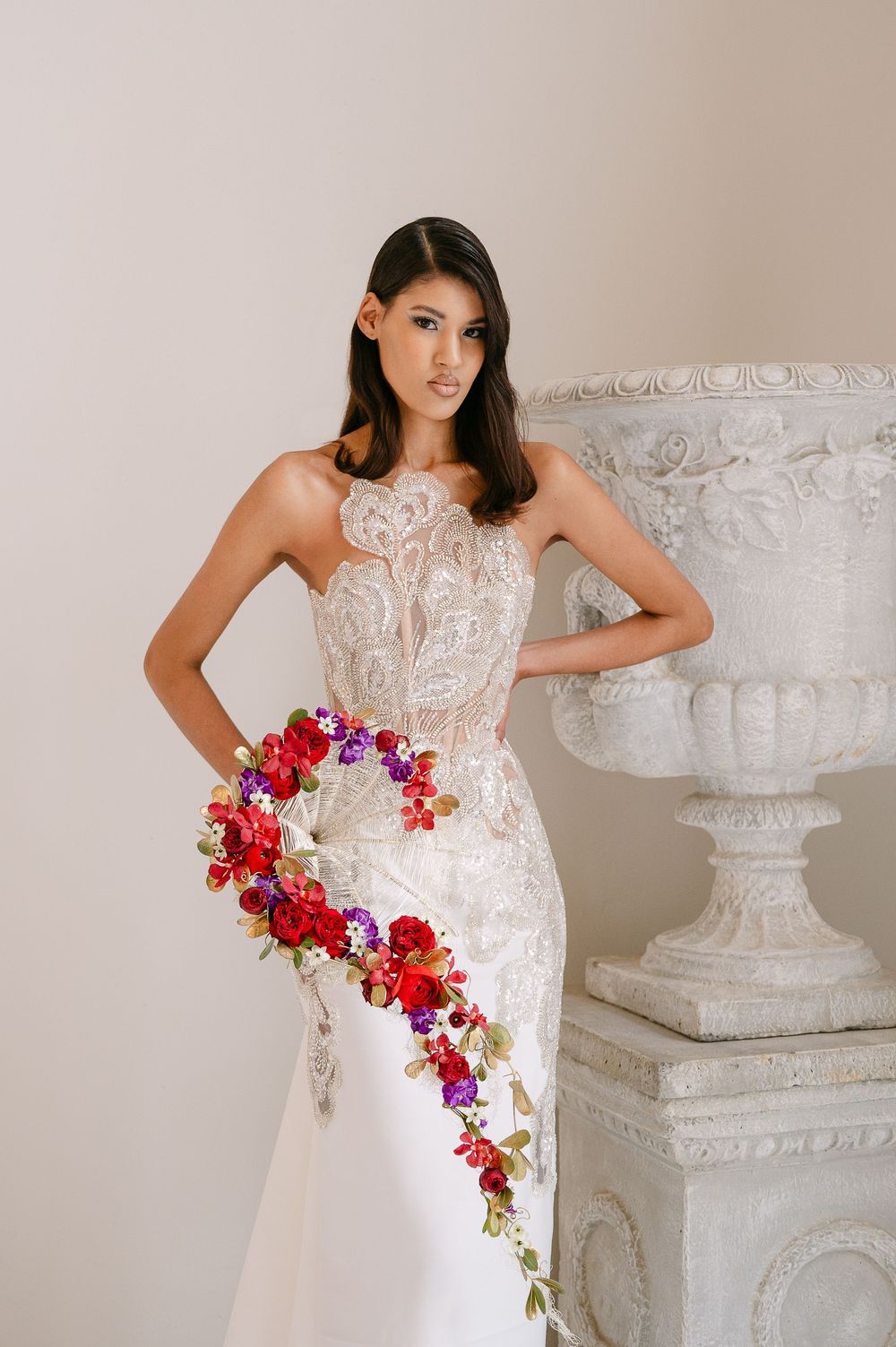 Bridal portrait featuring flowing white dress with lace details and vibrant red and purple cascading floral arrangement.