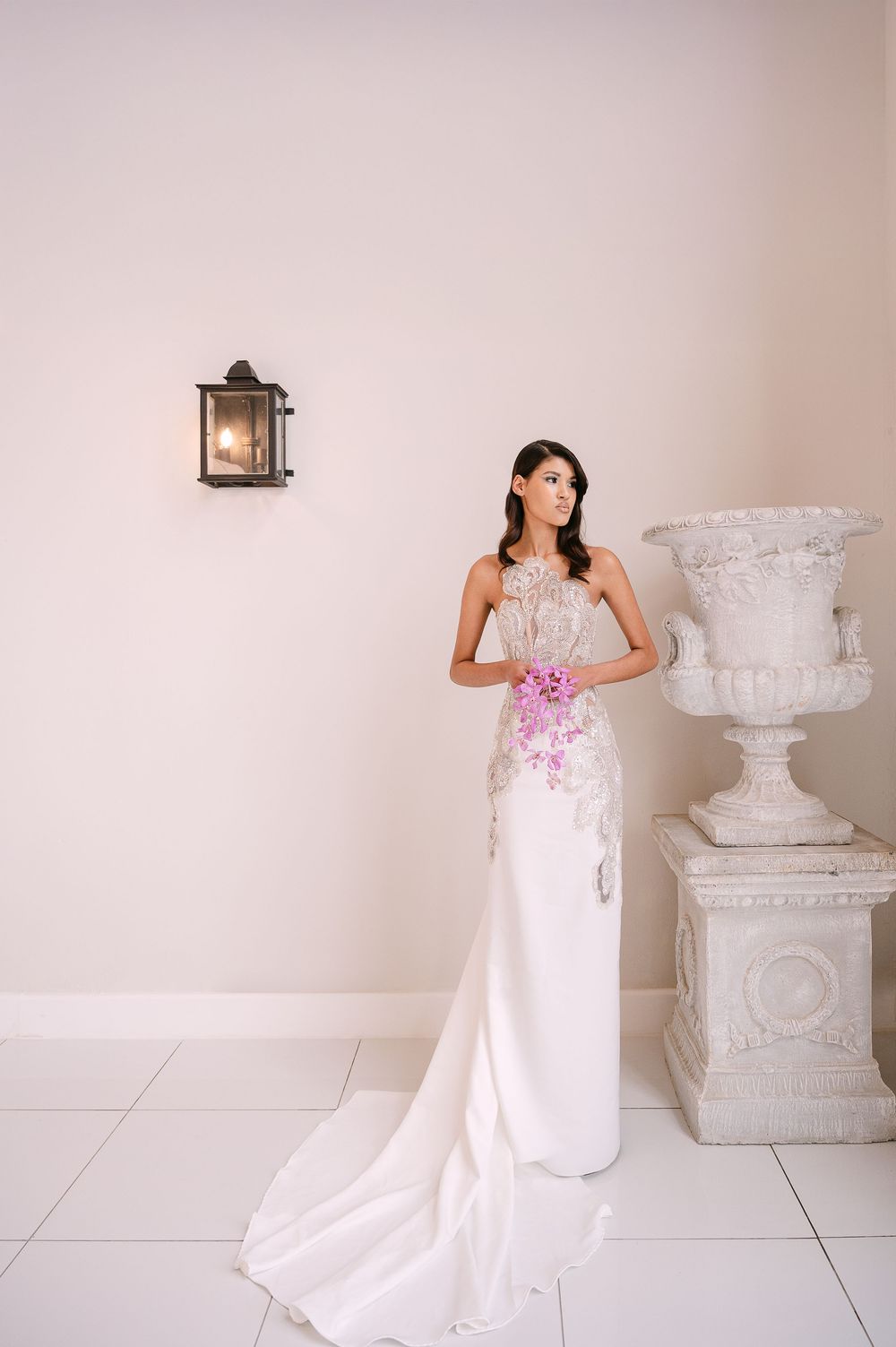 Beautiful white trumpet wedding gown with pink floral accents displayed against a light neutral background.