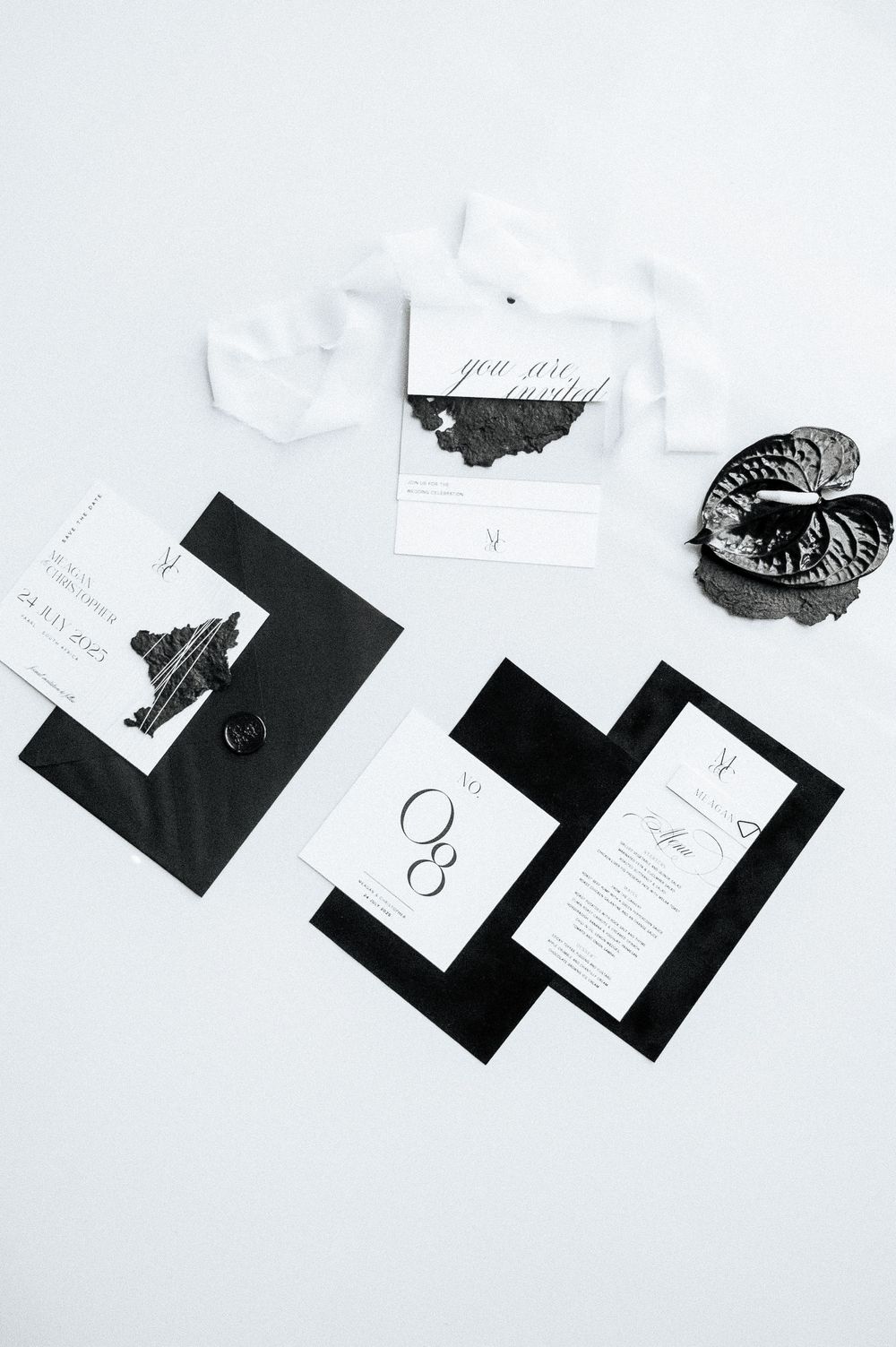 A minimalist black and white product photography layout featuring scattered paper cards and labels on a white surface.
