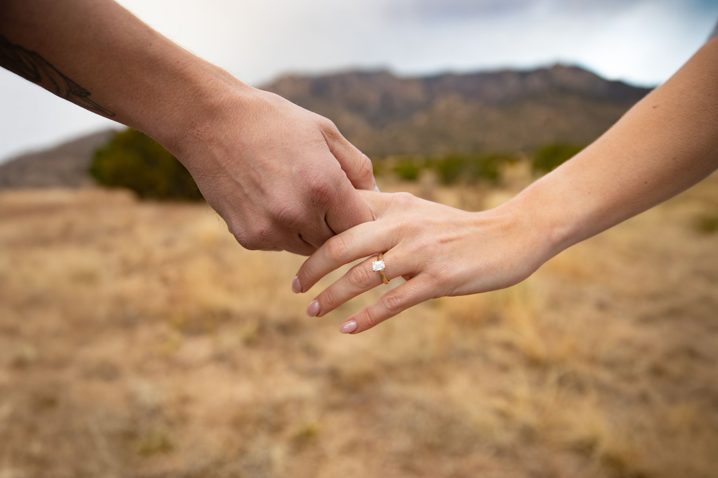 Two people holding hands while walking on a sandy beach at sunset with ocean waves in the background.