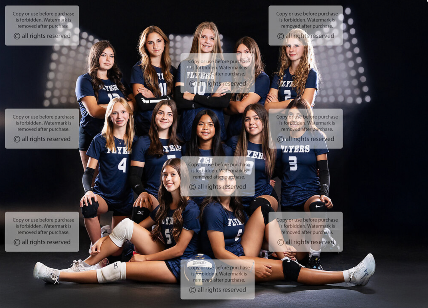 Volleyball team photo shoot with players in navy uniforms against dark backdrop.