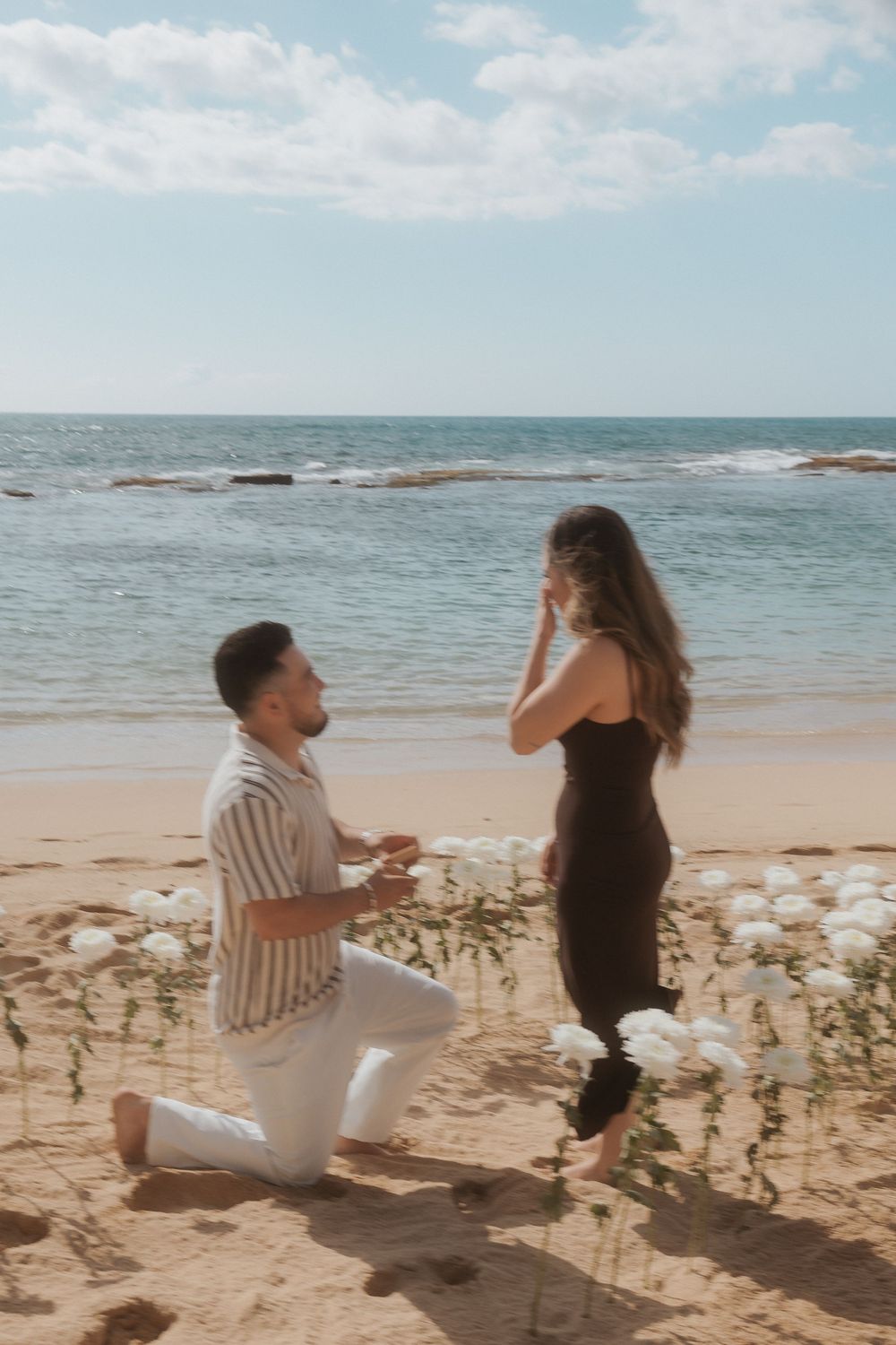 A romantic beach proposal scene with flowers arranged in front of an ocean backdrop.
